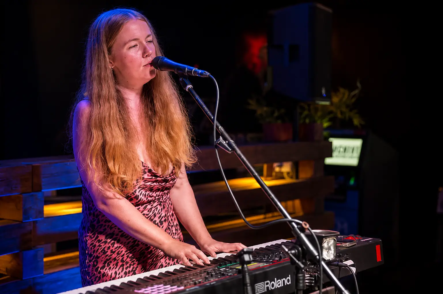 Jess Martyn singing at her keys in a low-lit bar, warm and blue lighting across the room