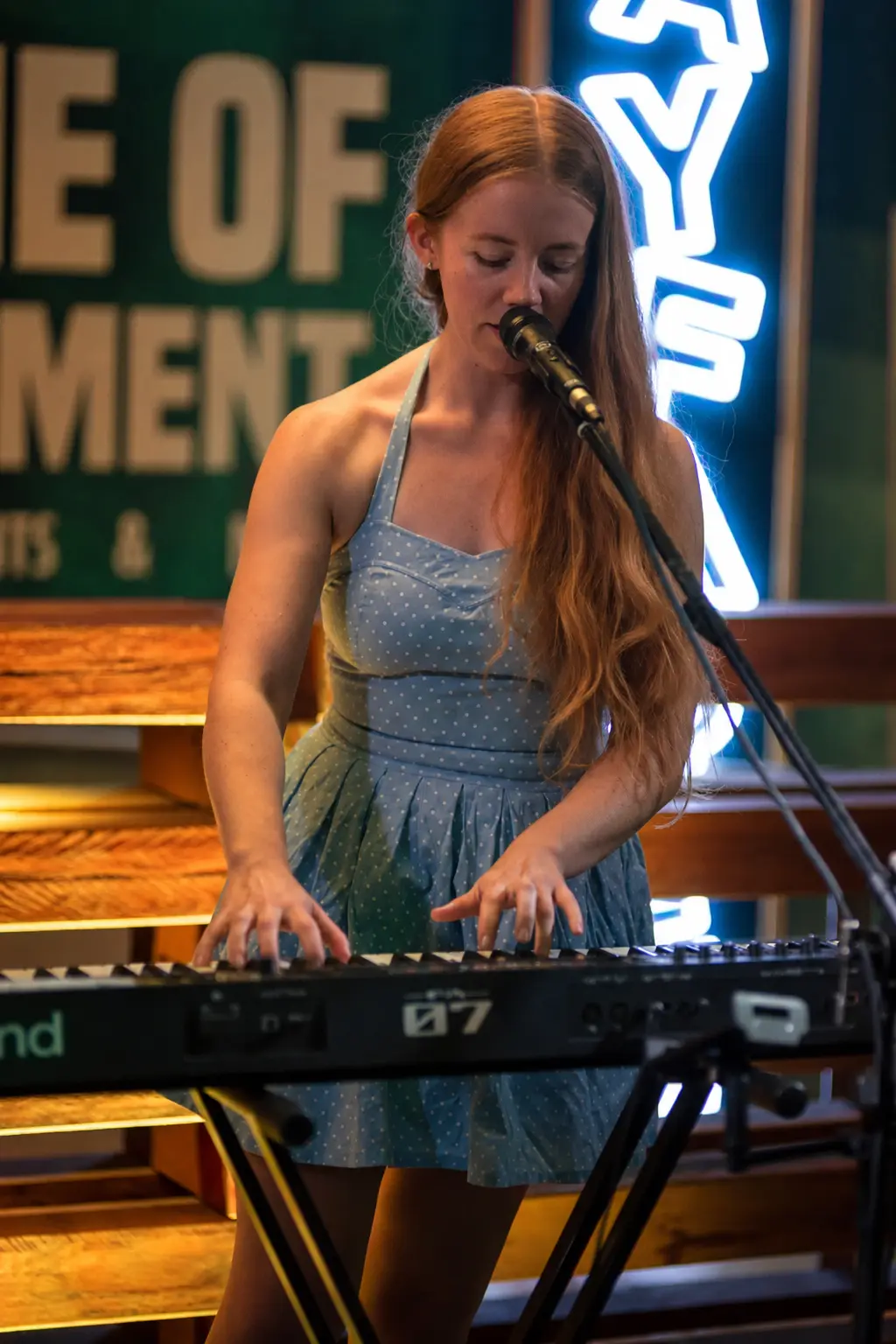 Jess Martyn playing her keys at a Brisbane venue, mic on a boom stand, neon sign glowing behind her