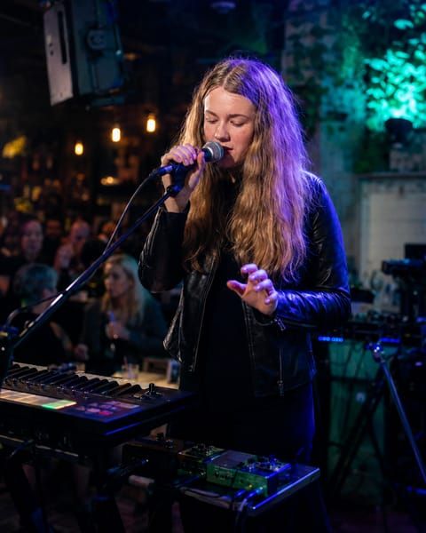Jess Martyn singing into the mic with her loop-pedal rig at a busy Brisbane pub