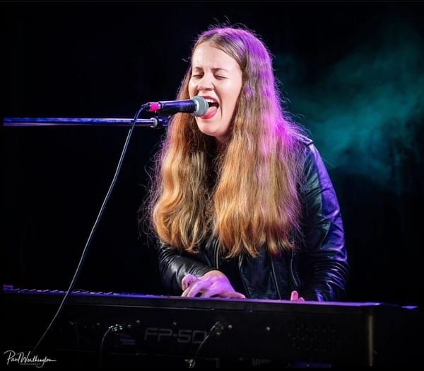 Jess Martyn mid-song at the keyboard, stage lights behind