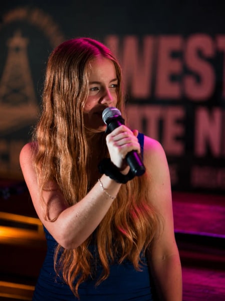 Jess Martyn singing into a handheld mic on a West End stage under pink and orange lights
